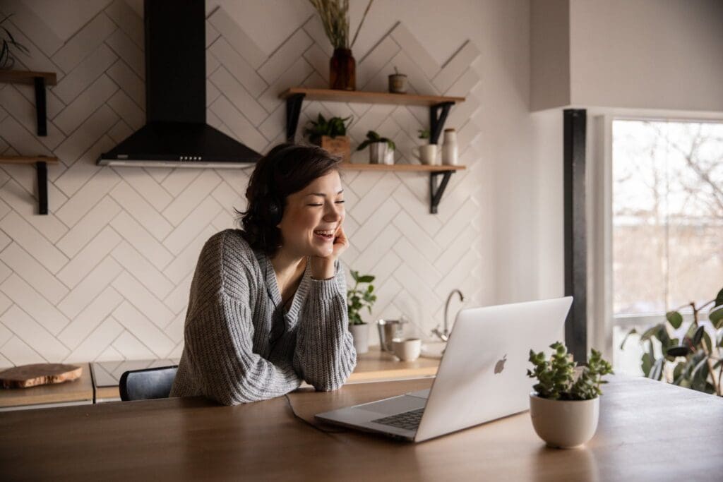 gig image seo for a Young cheerful female smiling and talking via laptop while sitting at wooden table in cozy kitchen